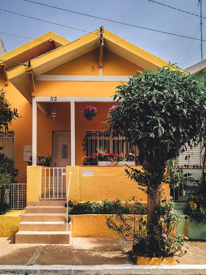 pexels-photo-2102587 Bright yellow house with lush garden, vibrant flowers, and welcoming porch entrance.
